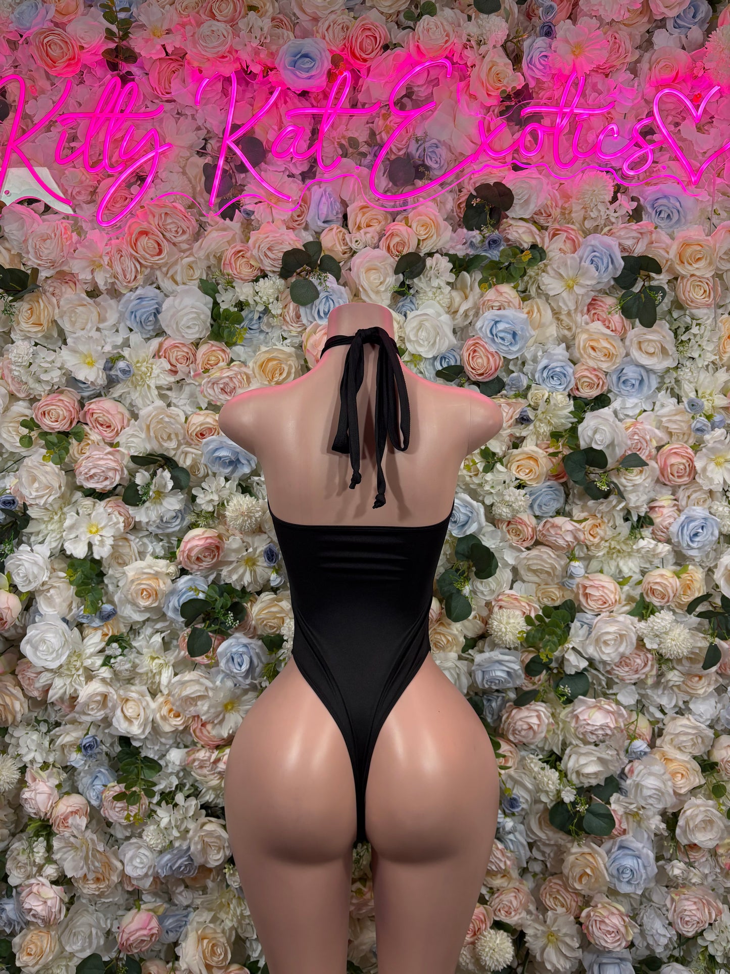 Black one-piece bodysuit with open back and tie straps; high-leg coverage