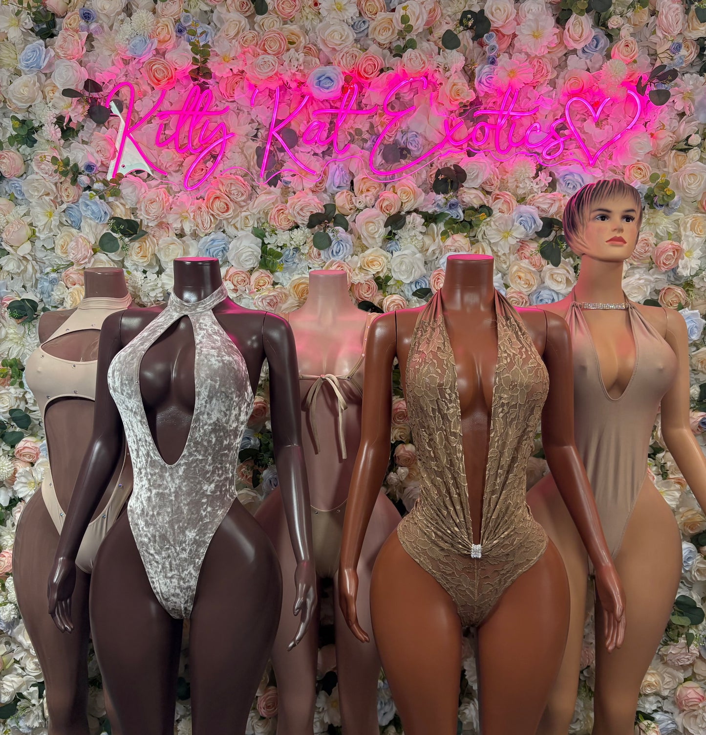 Tan one-piece bodysuit with deep V neckline on mannequin among other bodysuits
