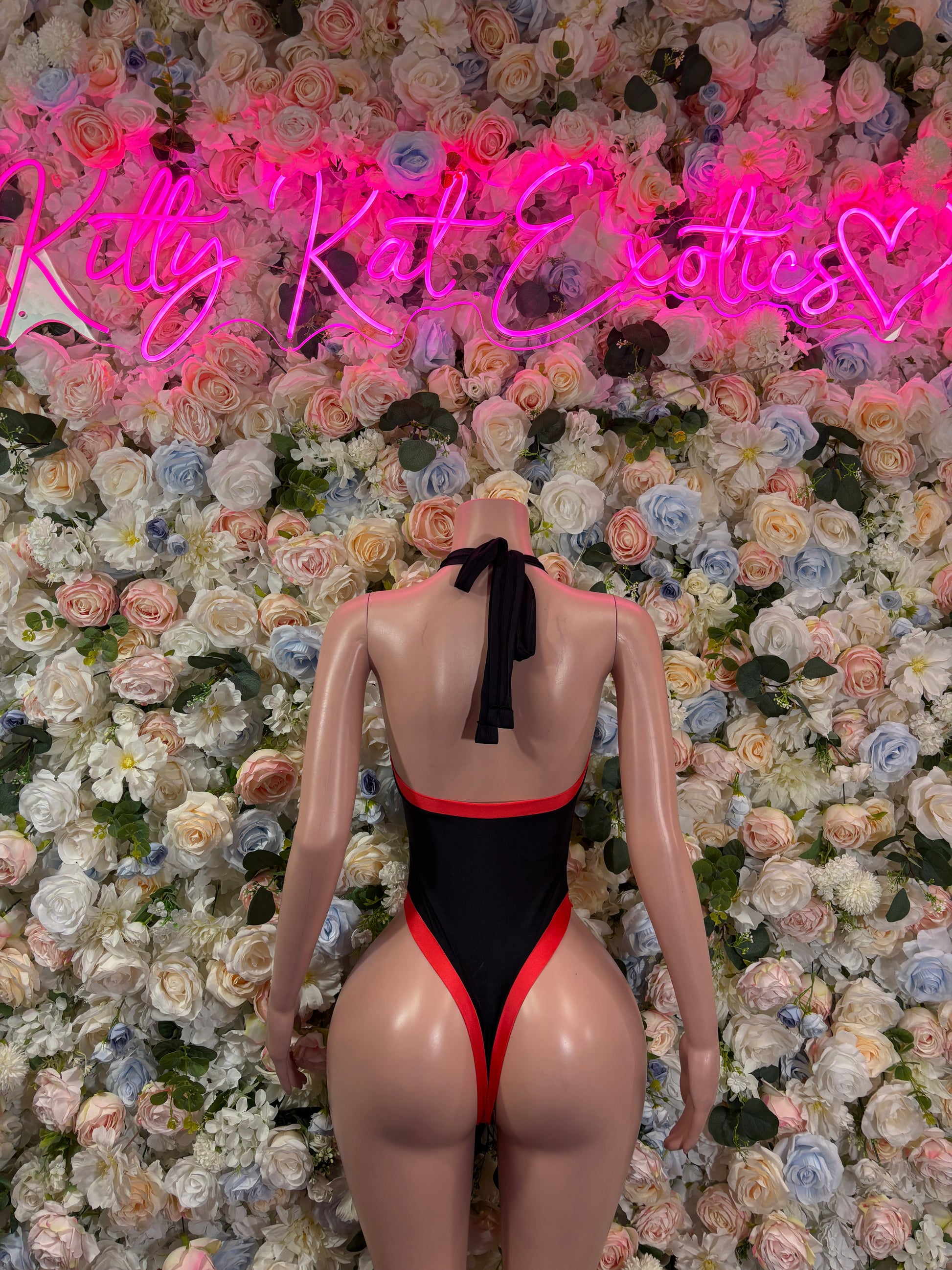Black one-piece bodysuit with red trim and tied bow on open back.