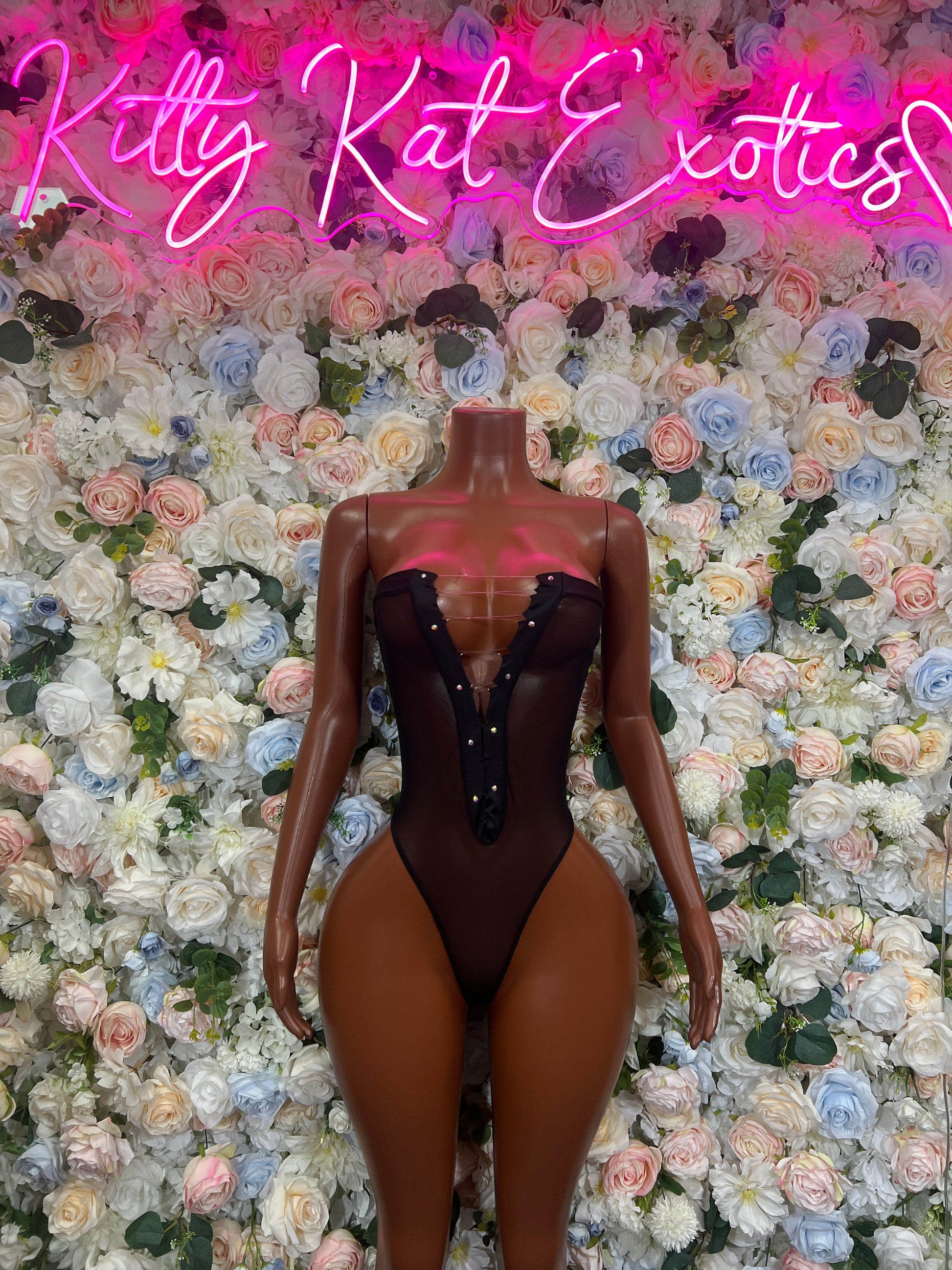 Black mesh one-piece bodysuit with vertical lace-up detail and high-cut legs on mannequin.