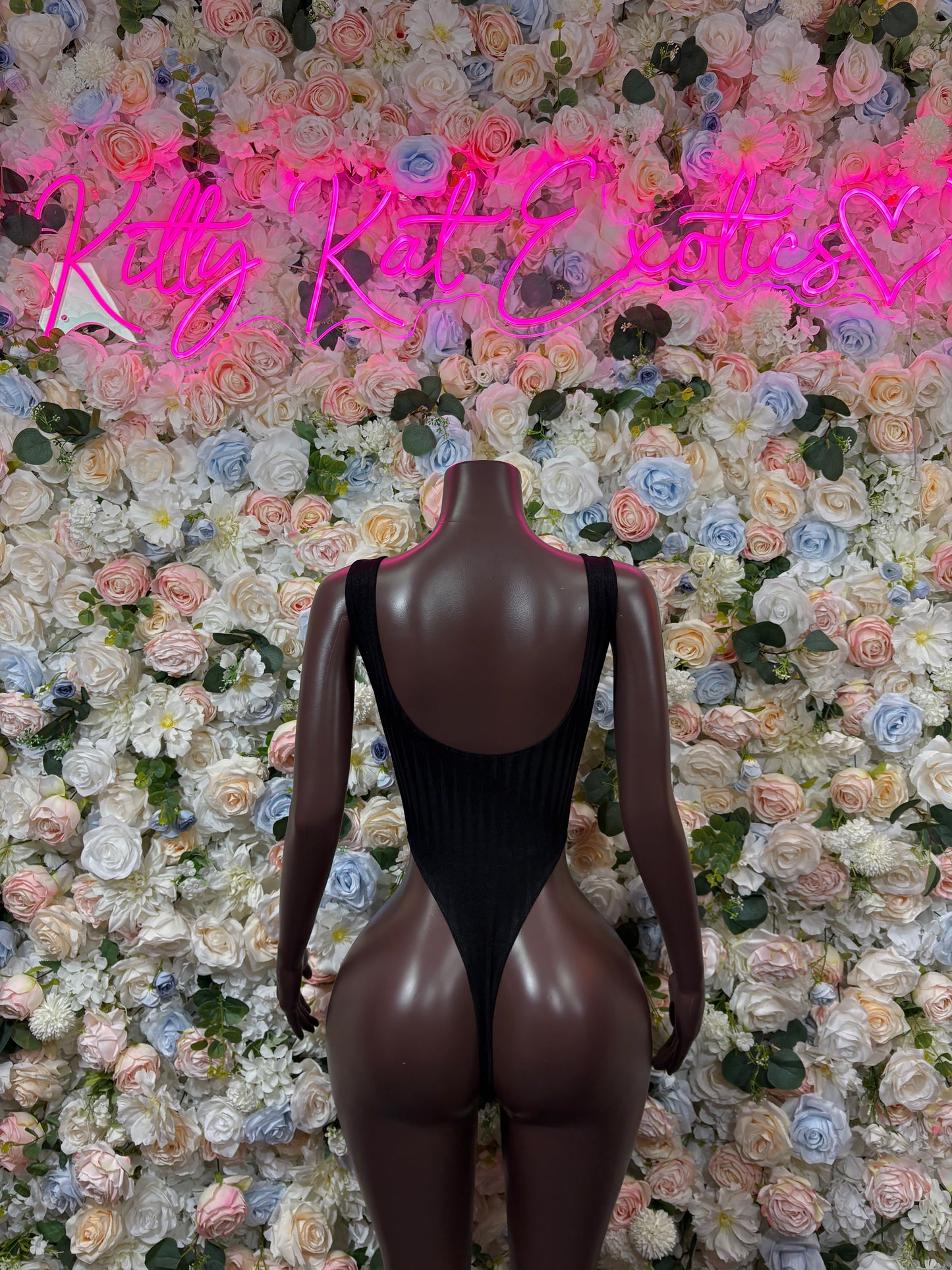 Black one-piece bodysuit with open back, stud-trim straps, and long sleeves.