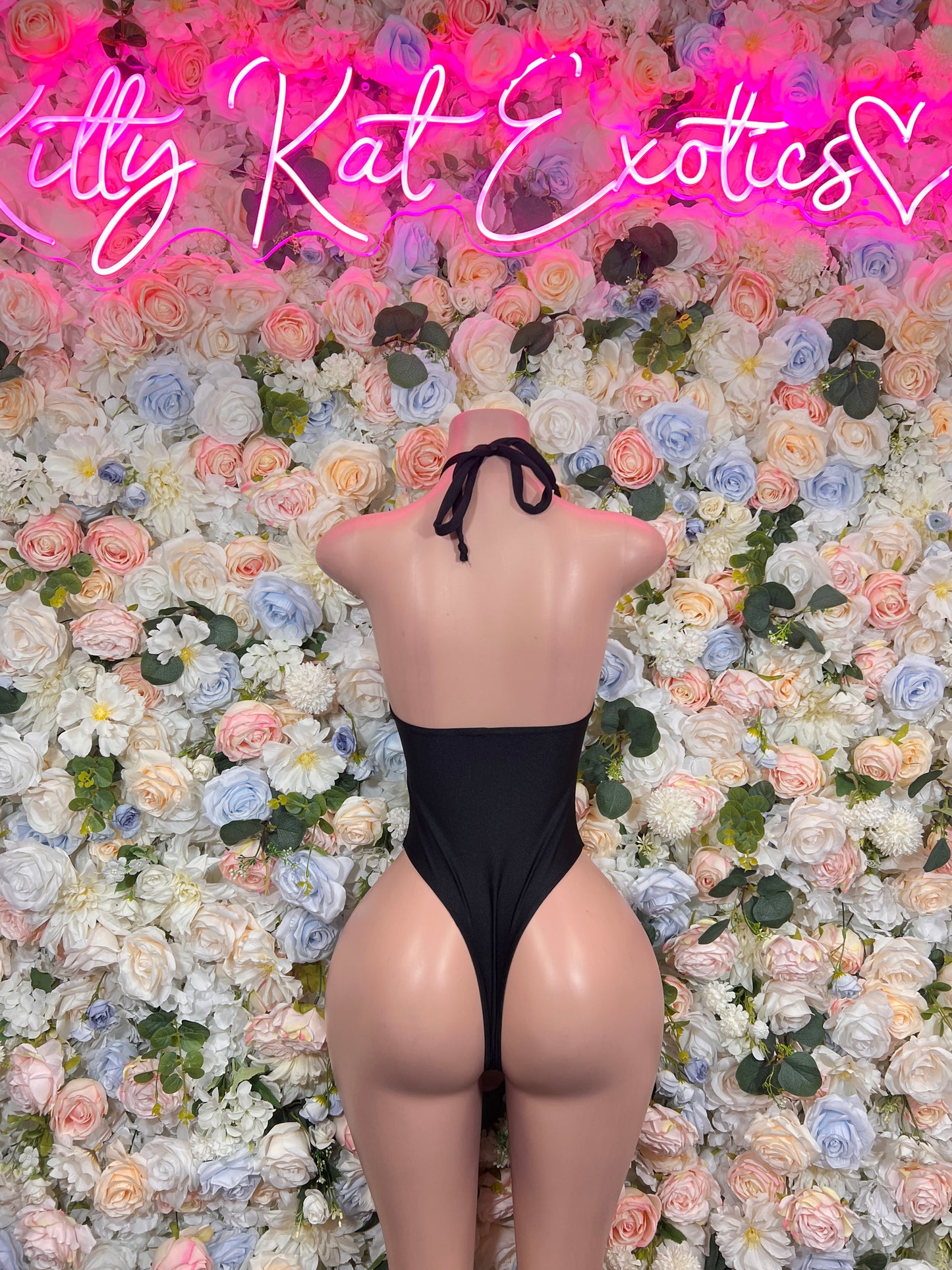Black one-piece bodysuit with low back and crossed straps, high-leg cut.