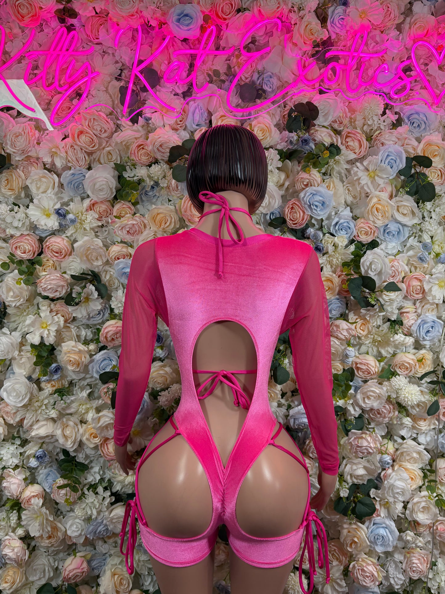 Pink velvet bodysuit with open back, crisscross straps, and long sleeves