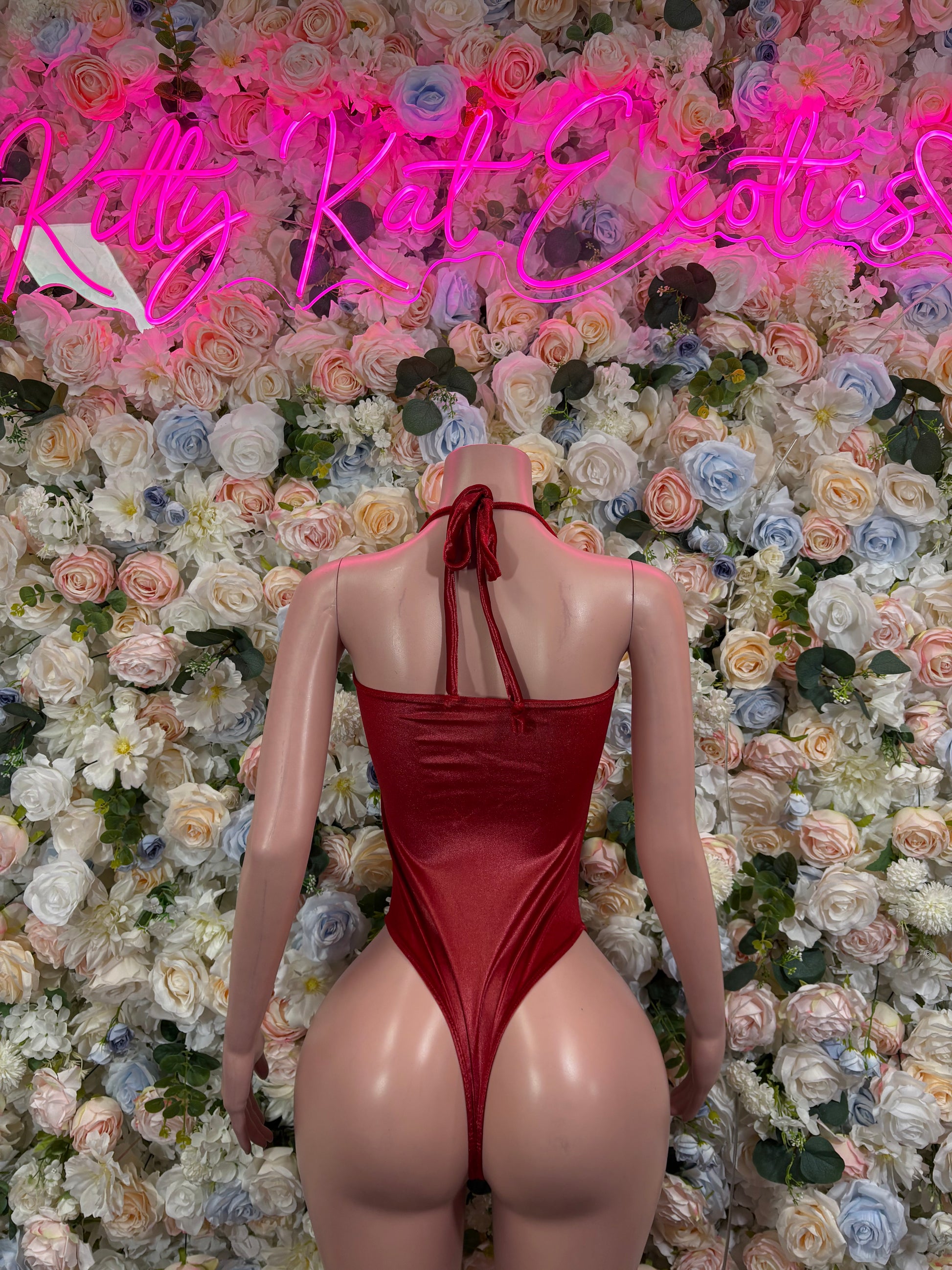 Burgundy satin bodysuit with open back, thin crisscross straps, and high-leg cut