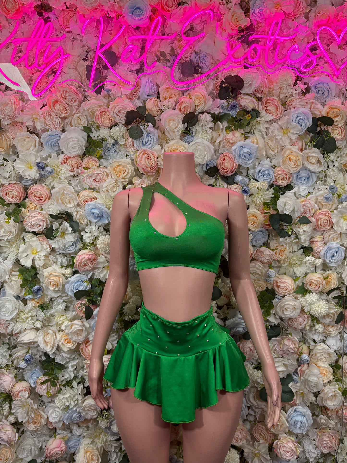 Green two-piece skirt set with strappy crop top and ruffled mini skirt on mannequin.