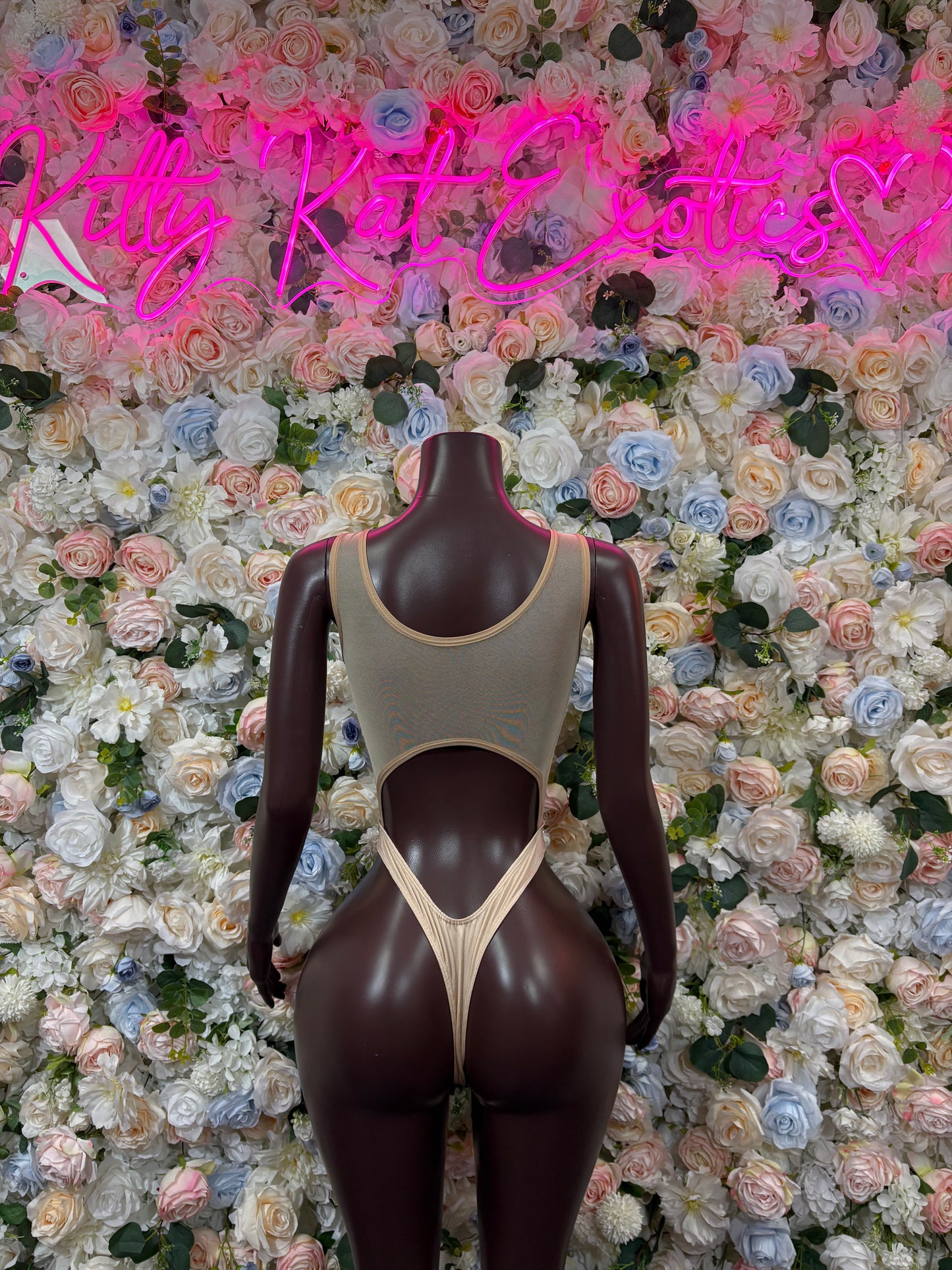 Nude one-piece bodysuit on mannequin with halter-style straps and backless design