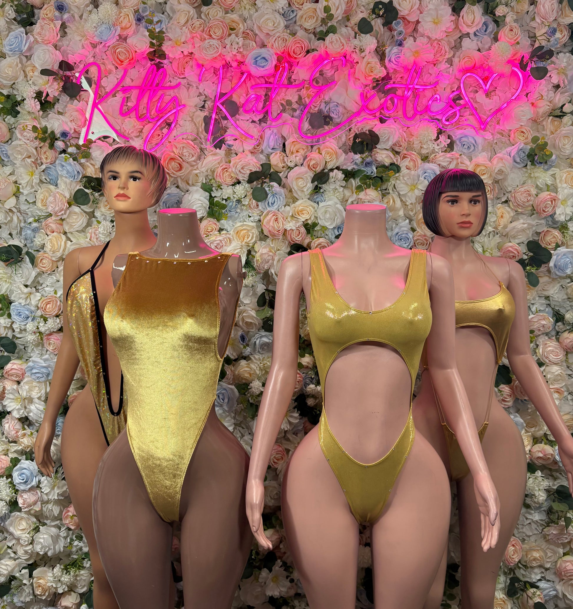 Gold one-piece bodysuits on three mannequins with scoop neck and high-cut legs
