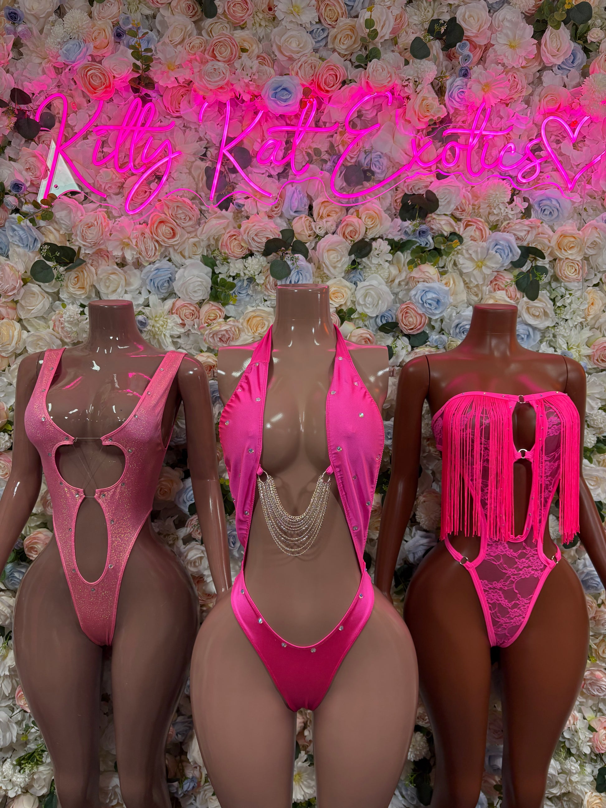 Hot pink one-piece bodysuits on mannequins, including fringe and cutout styles