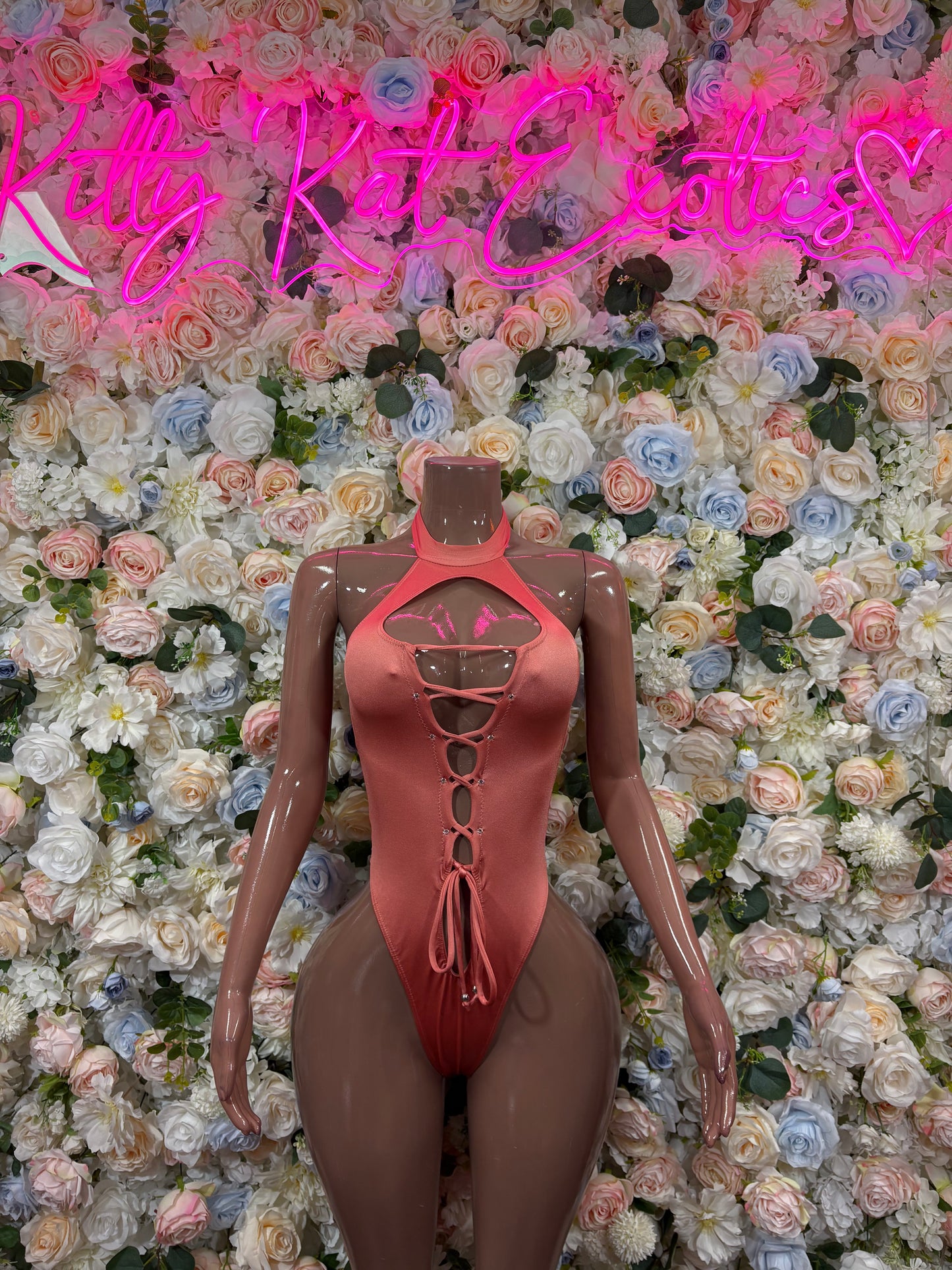 Rose-pink lace-up bodysuit with halter straps and cutout front; high-cut legs.