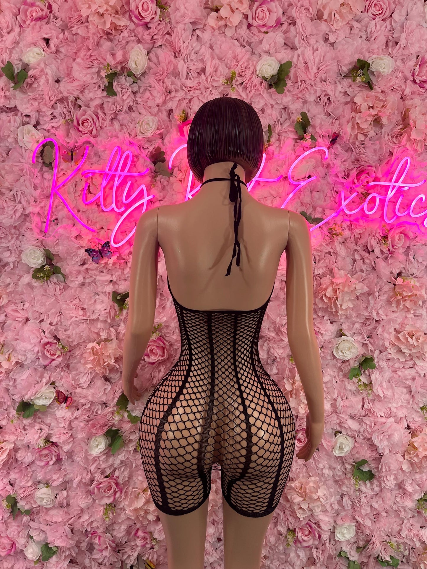 Mannequin wearing Valentines Day One Piece Fishnet Black Dancewear Exotic wear against a backdrop of pink and white roses with neon sign lighting.