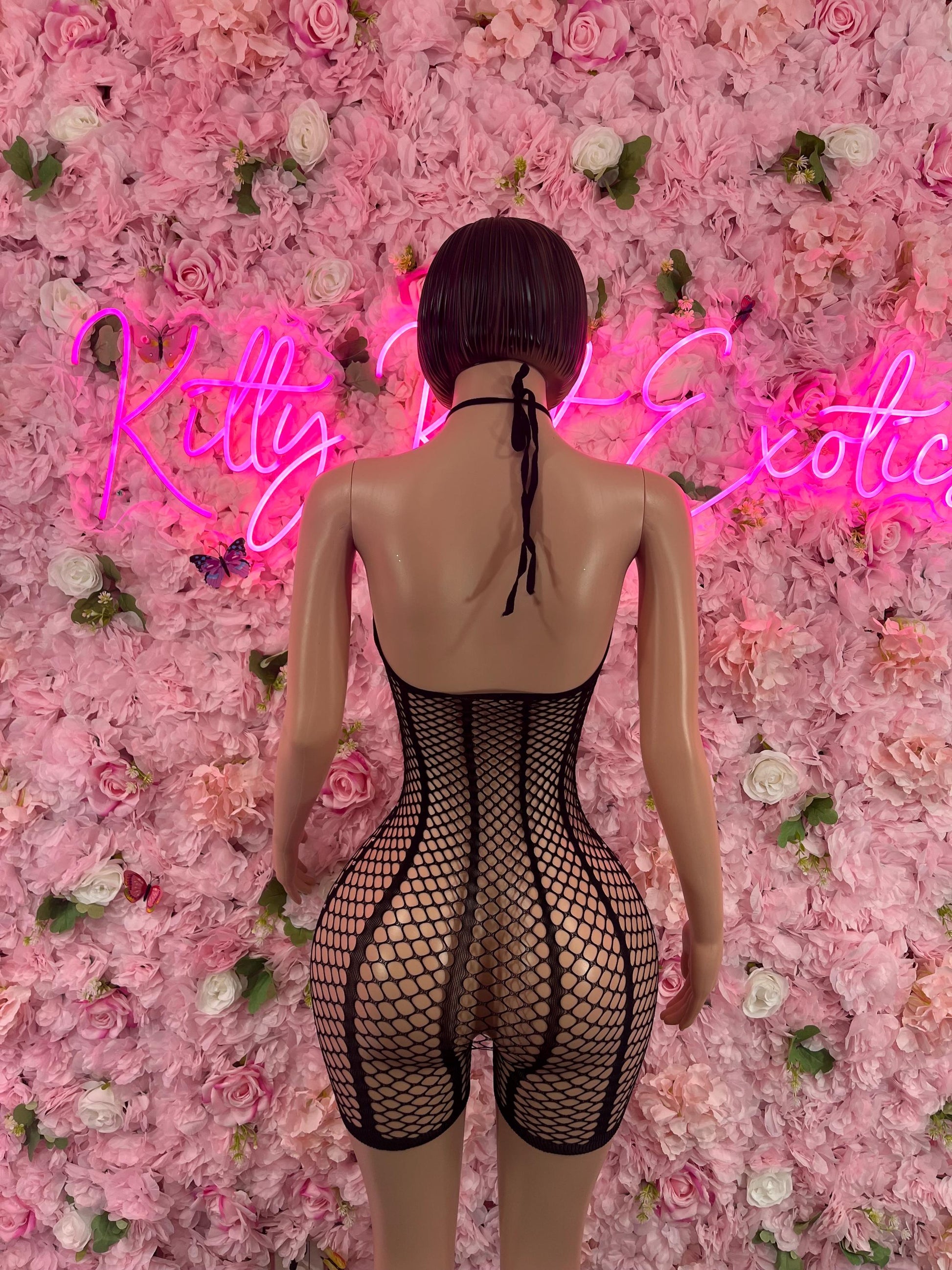 Mannequin wearing Valentines Day One Piece Fishnet Black Dancewear Exotic wear against a backdrop of pink and white roses with neon sign lighting.