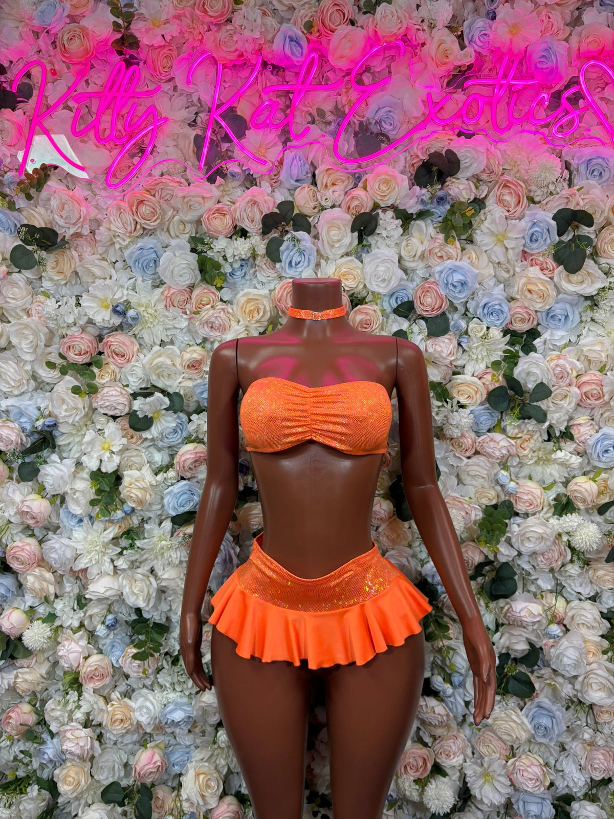 Orange ruched bandeau top with ruffled mini skirt set on mannequin