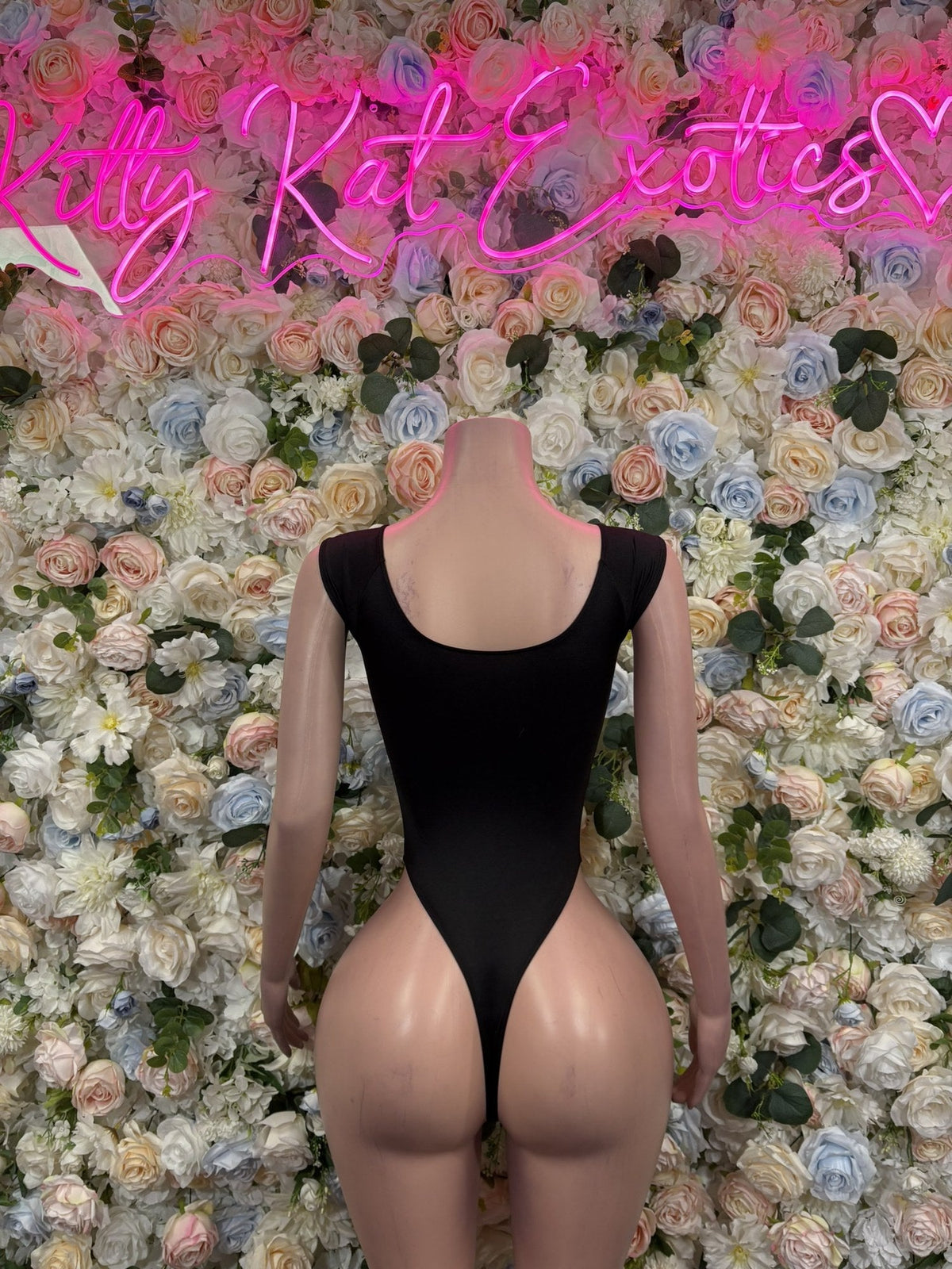 Back of a black long-sleeve bodysuit with a low scoop neckline and high-cut legs.