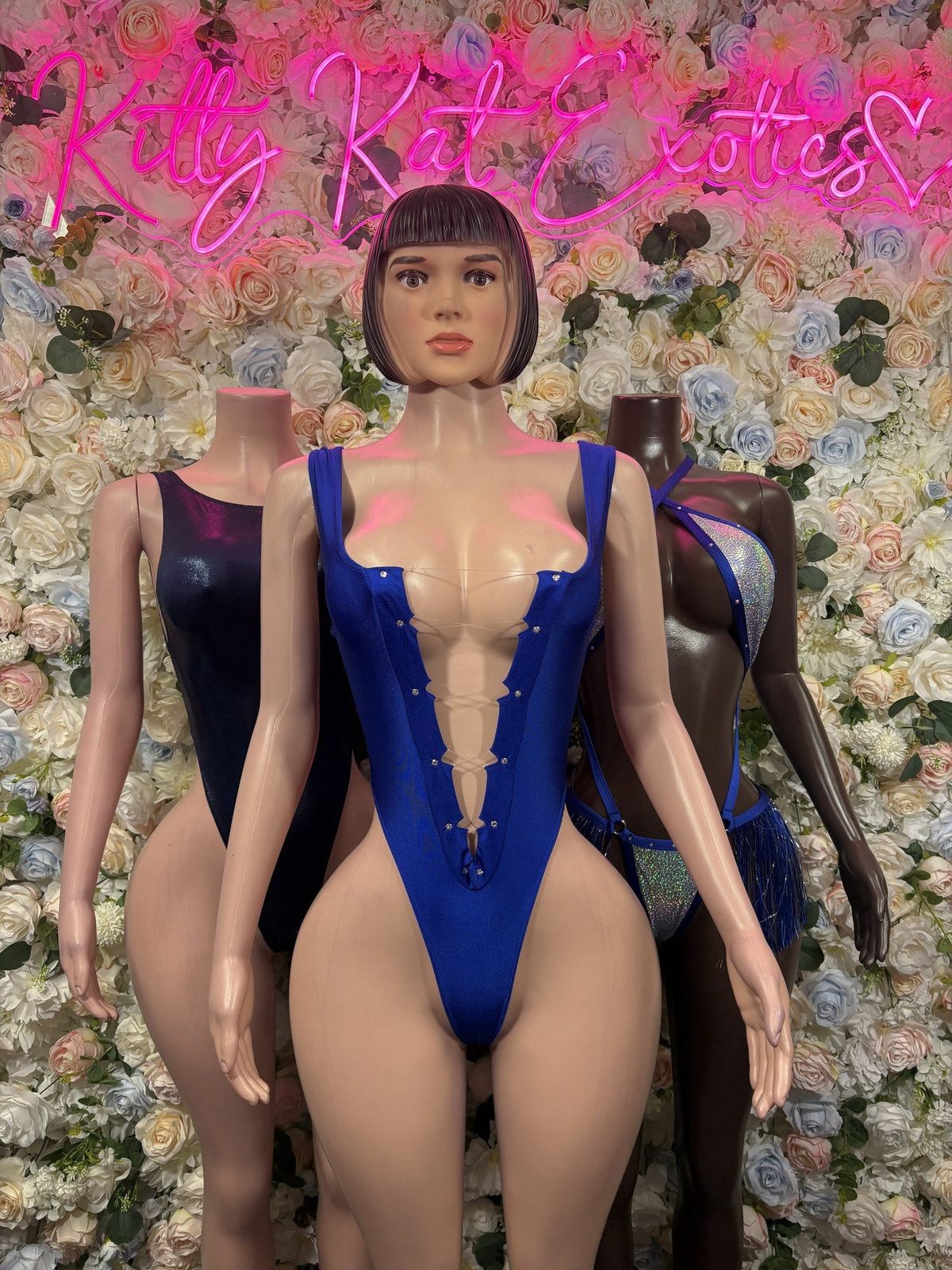 Royal blue strappy cutout bodysuit with glitter panels and hip fringe, partially visible behind another mannequin